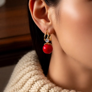 Detail of elegant gold ear hoop with a red resin bead pendant and sparkling zircon stone