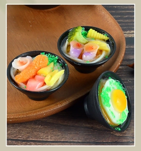Detail of three miniature Japanese udon noodle bowls with realistic resin toppings on a wooden tray