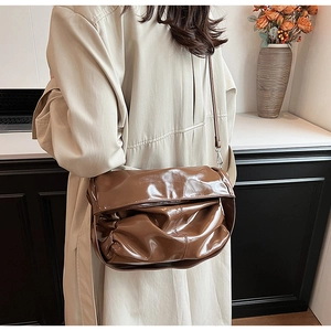 Detail of dark brown glossy patent leather shoulder bag with stylish pleated texture