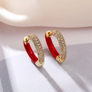 Macro view of gold hoop earrings with sparkling zircons and red enamel inlay details