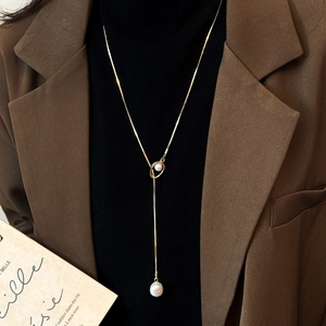 Detail of elegant gold Y-shaped necklace with pearls worn on a stylish black turtleneck