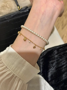 Detail of layered gold bracelet set featuring heart charms, star gems, and white pearls