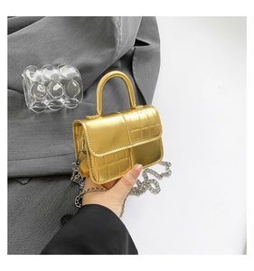 Detail showing hand-held golden mini crossbody bag with crocodile texture and metal chain