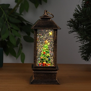 Macro detail of a bronze lighted Christmas lantern featuring a snowy tree decoration inside