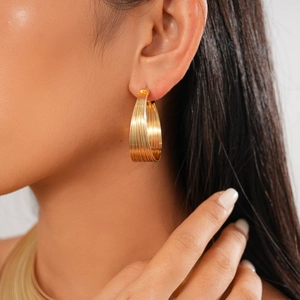 Close-up of gold layered hoop earrings with textured metallic stripes on a female model