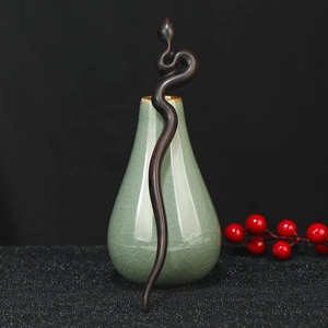 Detail of snake-shaped dark sandalwood hair pin leaning on a celadon vase with red berries