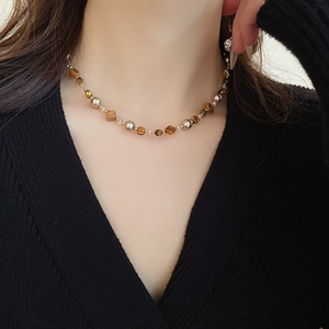 Detail der Perlenkette aus Tigerauge und Muschelperle an Model mit schwarzem V-Ausschnitt