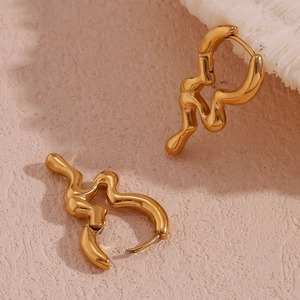 Close-up of gold irregular liquid metal hoop earrings on textured beige surface