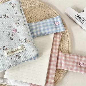 Close-up of floral and plaid cotton notebook covers with snap buttons on a woven mat
