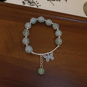 Macro shot of green beaded bracelet with hollow butterfly charm on a wooden base