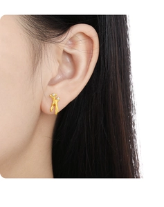 Close-up of a model wearing a gold abstract human-shaped earring with small diamonds