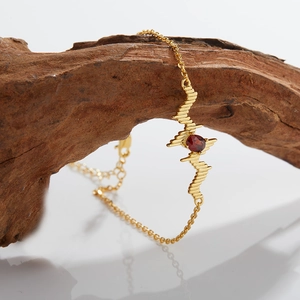 Macro view of gold silver necklace with red gemstone and heartbeat wave on wood