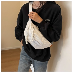 Detailed shot of white canvas crossbody bag with letter embroidery worn by a model