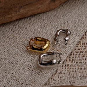Close-up of three U-shaped S925 silver and gold thick hoop earrings on a wooden base