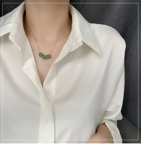 Close-up of a gold necklace with three green jade beads worn by a model in a white shirt