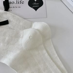 Close-up of white ribbed knit socks featuring a delicate black ribbon bow detail