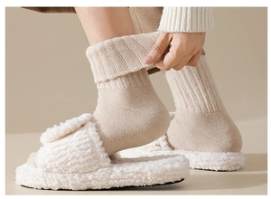 Detail view of thick beige wool socks worn with plush slippers showing knit texture