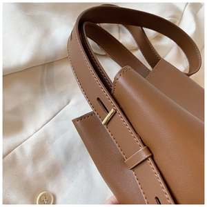Detail shot of brown leather bucket bag showing precise stitching and gold metal buckle