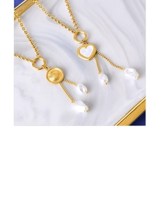 Détail de colliers dorés avec pendentifs en nacre et perles baroques sur plateau céramique