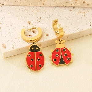 Detail of gold-plated ladybug earrings with red enamel on a textured stone base