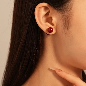 Boucles d'oreilles boules en résine rouge foncé au design épuré sur modèle