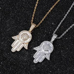 Macro shot of gold and silver Hamsa Hand pendants with micro-pave stones on twist chains