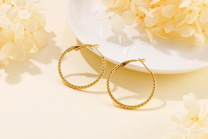 Detailed close-up of gold hoop earrings with textured finish on a white ceramic plate