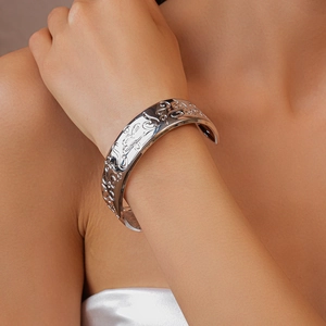 Detail of silver embossed oval cuff bracelet with intricate relief patterns on model