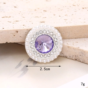 Detail view of a 2.5cm round charm with purple gemstone, rhinestones and pearls