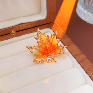 Detailed view of a gold-plated maple leaf brooch with orange enamel and zircon on a box