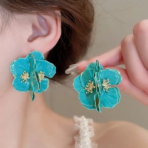 Gros plan d'un modèle portant de grandes boucles d'oreilles fleur bleue et émail doré