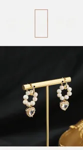 Detail of heart-shaped pearl hoop earrings with gold-plated metal on a black background