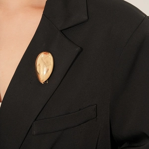 Detailansicht einer goldenen Tropfenbrosche am schwarzen Anzugrevers mit Glanzfinish