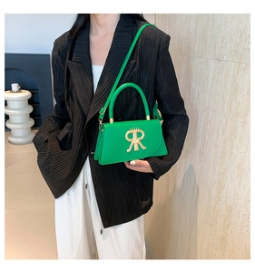 Detail of green square bag with golden R-shaped logo and elegant handle grip