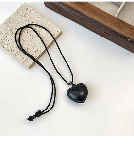 Détail d'un pendentif coeur noir avec cordon tressé sur un fond au design minimaliste chic