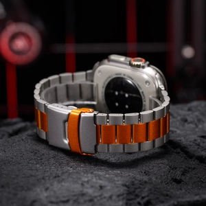Detail of silver-grey and orange titanium watch band with folding clasp on dark rock texture
