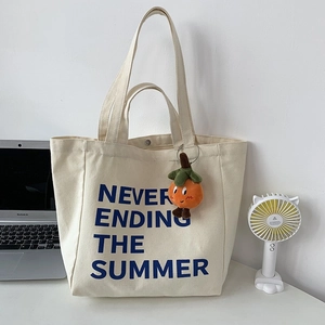 Detail of off-white canvas tote bag with navy blue lettering and plush vegetable charm