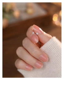 Macro shot of a tiny silver four-point star earring with a zircon stone on a fingertip