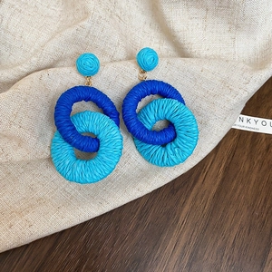 Detailed macro view of blue hand-woven raffia drop earrings on a rustic linen background