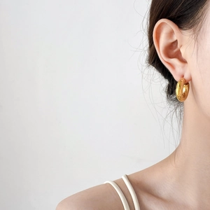 Close-up of model wearing thick chunky golden hoop earrings with high polish mirror finish
