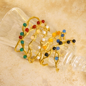 Golden wavy open cuff bracelet with colorful pearl beads displayed on crystal glass