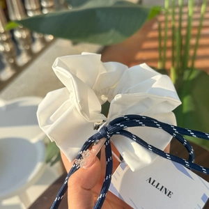 Detail of white cotton scrunchie with navy plaid bow and brand tag in sunlight