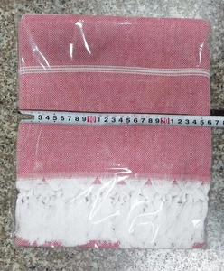 Detail view of red and white striped Turkish towel with fringe and measuring tape