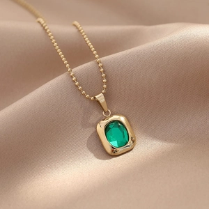 Elegant gold ball chain necklace with square green gemstone pendant on champagne satin