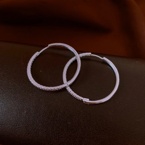 Detailaufnahme silberner strukturierter Creolen auf einem Vintage-Lederhintergrund
