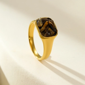 Macro detail of gold vintage square ring with dark natural stone inlay on beige texture