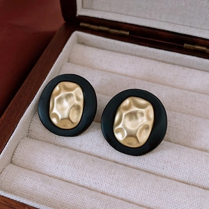Detail view of retro oval stud earrings with black matte finish and gold hammered metal center