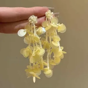 Close-up of cream yellow floral stud earrings with cascading long sequin tassels