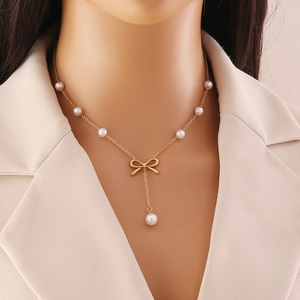 Elegant gold bow necklace with white pearl tassels on a model in a beige suit