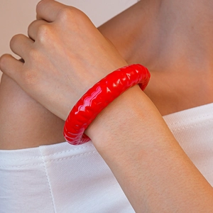 Dettaglio del bracciale largo in acrilico rosso acceso con trama plissettata ondulata al polso